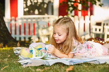 Image showing Cute Little Blond Girl Reading Book Outside on Grass