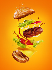 Image showing The hamburger with flying ingredients on orange background