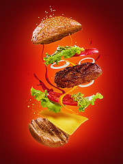 Image showing The hamburger with flying ingredients on red background