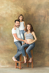 Image showing Pregnant mother with teen daughter and husband. Family studio portrait over brown background