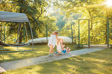 Image showing Cute little blond girls riding a toy car in summer.