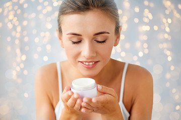 Image showing close up of happy woman holding and smelling cream