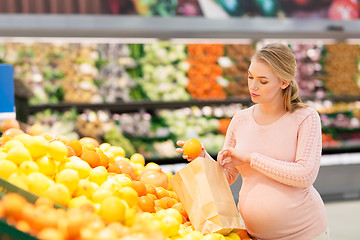 Image showing pregnant woman with bag buying oranges at grocery