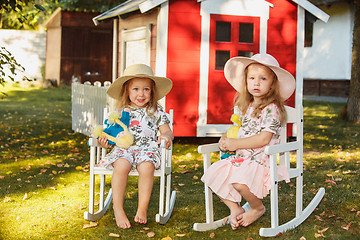 Image showing Cute little blond girls in hats sitting on the field with soft toys in summer.