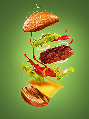 Image showing The hamburger with flying ingredients on green background