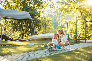 Image showing Cute little blond girls riding a toy car in summer.