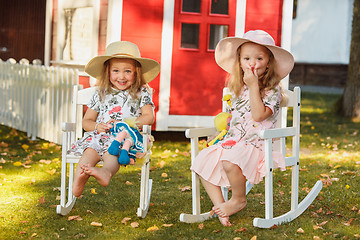 Image showing Cute little blond girls in hats sitting on the field with soft toys in summer.