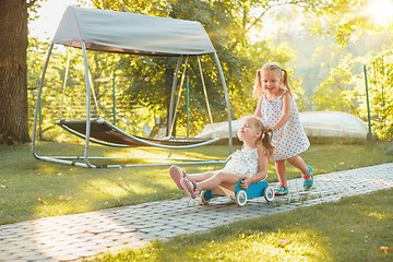 Image showing Cute little blond girls riding a toy car in summer.