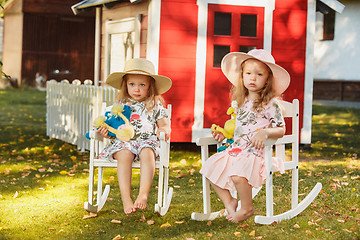 Image showing Cute little blond girls in hats sitting on the field with soft toys in summer.