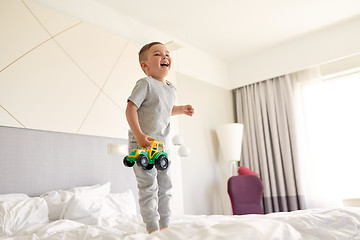 Image showing happy little boy with toy car on home or hotel bed