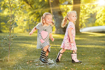 Image showing Cute little blond girls in hats sitting on the field with soft toys in summer.