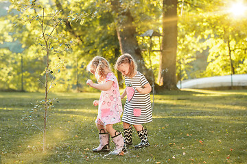 Image showing The cute little blond girls in rubber boots playing with water splashes on the field in summer