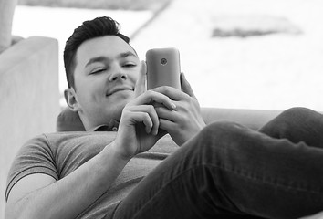 Image showing Young man using mobile while lying on couch