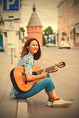 Image showing fun smiling woman with a guitar sits on the curb