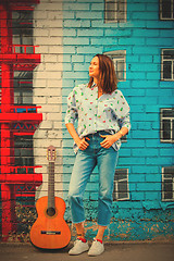 Image showing smiling woman in jeans and a blue shirt stands against the wall 