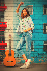 Image showing smiling woman in jeans stands near wall with graffiti next to gu