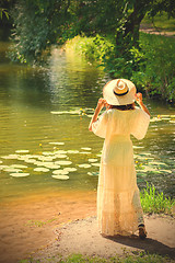 Image showing girl in a white dress and hat on the shore of a pond with water-