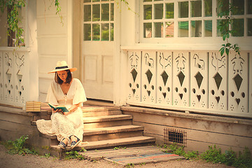 Image showing woman in a white dress and a straw hat reading a book on the por