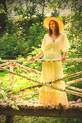 Image showing Beautiful woman in a white summer dress and a straw hat stands o