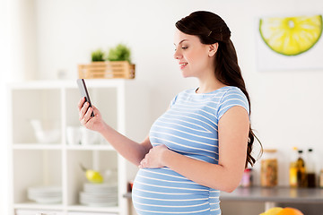 Image showing happy pregnant woman with smartphone at kitchen