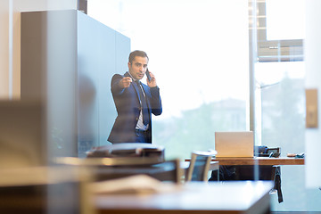 Image showing Businessman talking on a mobile phone in corporate office, pointing to camera.