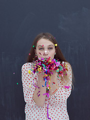 Image showing woman blowing confetti in the air isolated over gray