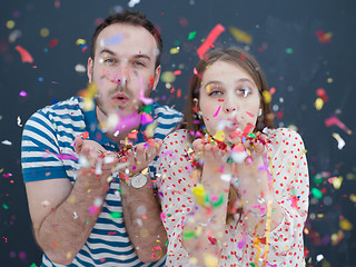 Image showing couple blowing confetti in the air isolated over gray