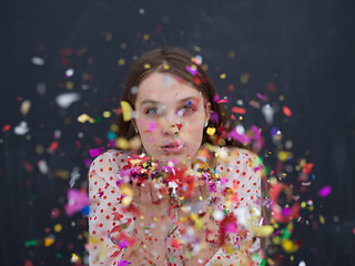 Image showing woman blowing confetti in the air isolated over gray