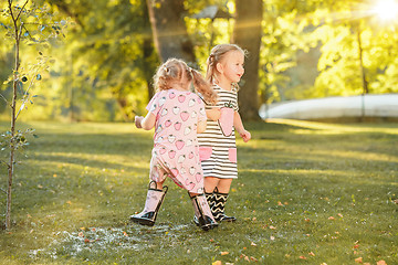 Image showing The cute little blond girls in rubber boots playing with water splashes on the field in summer