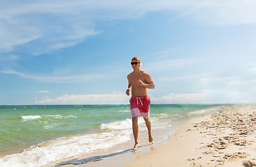 Image showing happy man with headphones running along beach