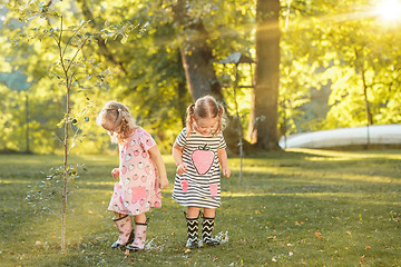 Image showing The cute little blond girls in rubber boots playing with water splashes on the field in summer