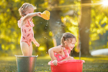 Image showing The cute little blond girls playing with water splashes on the field in summer