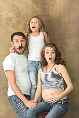 Image showing Pregnant mother with teen daughter and husband. Family studio portrait over brown background