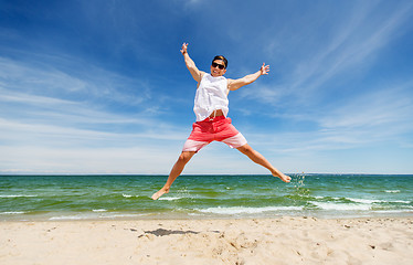 Image showing smiling young man jumping on summer beach