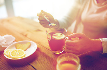 Image showing close up of woman adding honey to tea with lemon