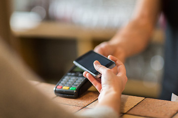 Image showing hands with payment terminal and smartphone at bar