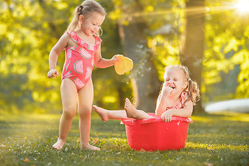 Image showing The cute little blond girls playing with water splashes on the field in summer