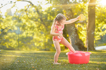 Image showing The cute little blond girl playing with water splashes on the field in summer