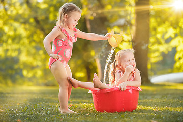 Image showing The cute little blond girls playing with water splashes on the field in summer