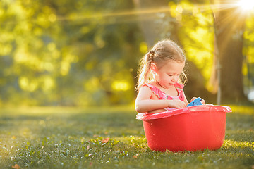 Image showing The cute little blond girl playing with water splashes on the field in summer