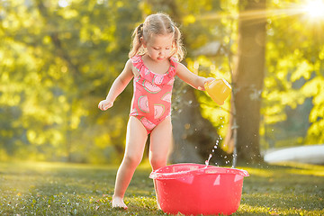 Image showing The cute little blond girl playing with water splashes on the field in summer