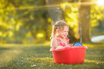 Image showing The cute little blond girl playing with water splashes on the field in summer