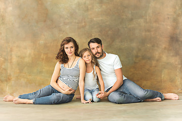 Image showing Pregnant mother with teen daughter and husband. Family studio portrait over brown background