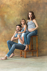 Image showing Pregnant mother with teen daughter and husband. Family studio portrait over brown background