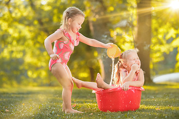 Image showing The cute little blond girls playing with water splashes on the field in summer