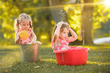 Image showing The cute little blond girls playing with water splashes on the field in summer