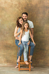 Image showing Pregnant mother with teen daughter and husband. Family studio portrait over brown background