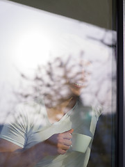 Image showing young man drinking morning coffee by the window