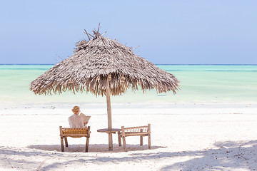 Image showing Women relaxing on dack chair under wooden umbrella on tropical beach.