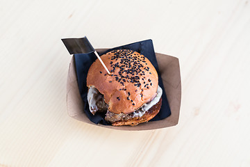 Image showing Hamburger on wooden table, one bite taken out of it.